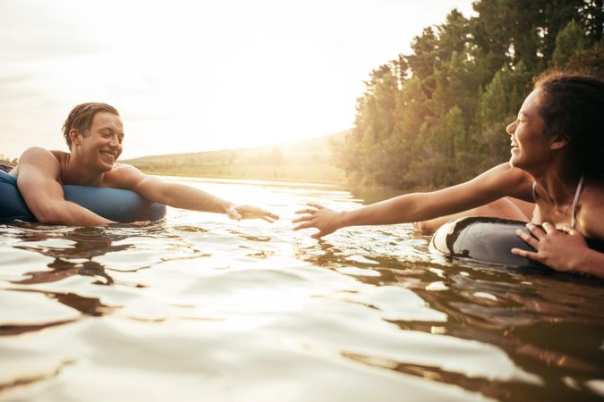 Affectionate young couple about to hold hands while floating on inner tubes in water