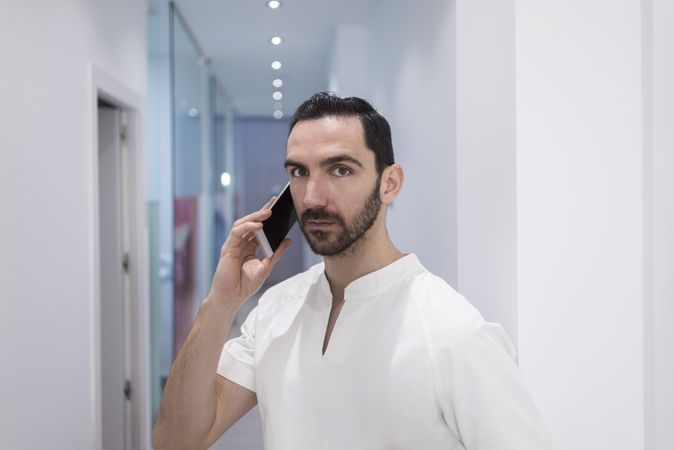 Bearded medical professional talking using a smartphone at hospital