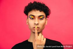 Male in rainbow eye make up gesturing silence, with finger on lips 41aYZ4