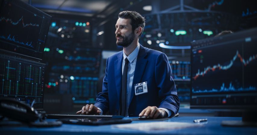 Adult Stock Exchange Broker Working on a Desktop Computer with Real-Time Stock Information, Commodities and Exchange Market Charts.