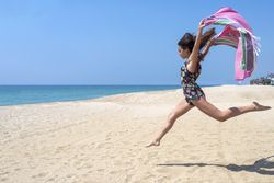 Woman jumping in sand with sarong
