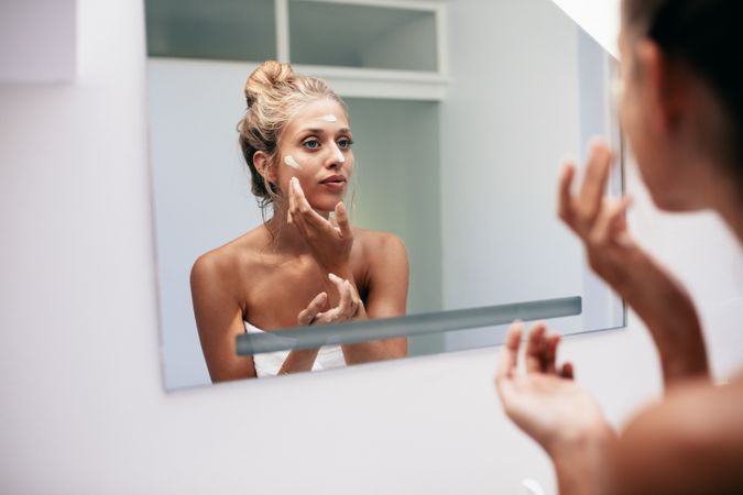Female looking into the bathroom mirror and putting on face cream