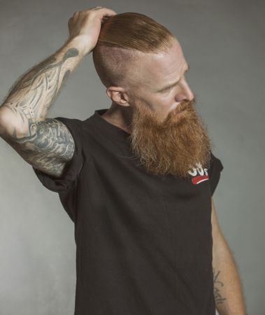 Confident adult red haired hipster touching hair and looking away