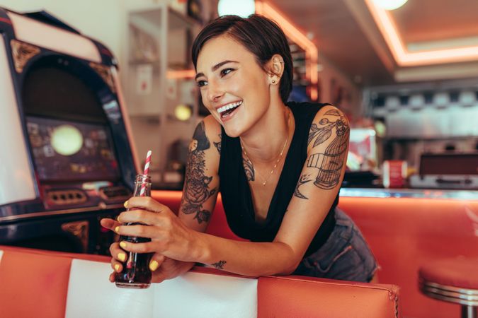 Smiling woman standing in a diner holding a soft drink looking away