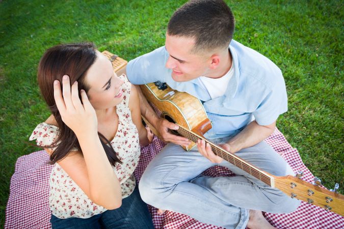 Young Adult Man Playing Guitar for His Girlfriend in the Park.