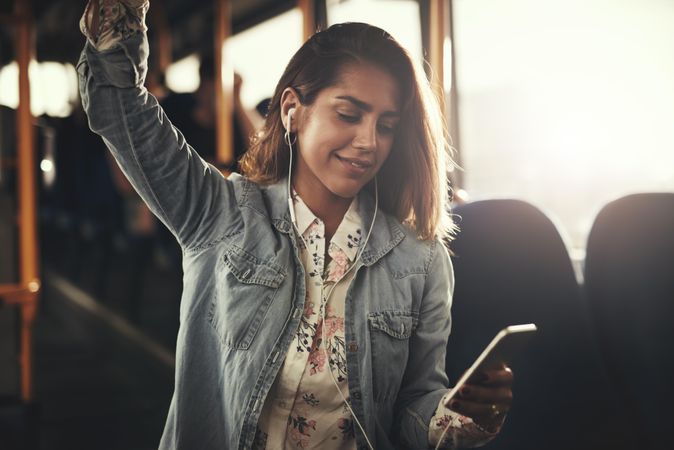 Woman listening to earbuds while standing on bus