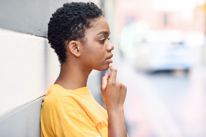 Black woman leaning on grey striped wall and looking in the distance