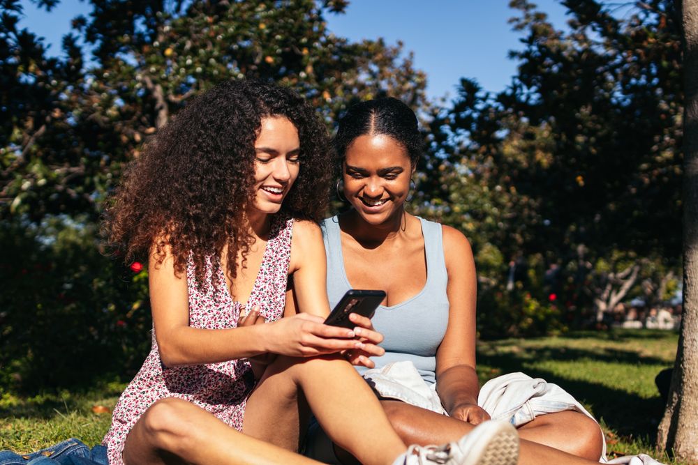 Black Latina friends using a smartphone in the park.