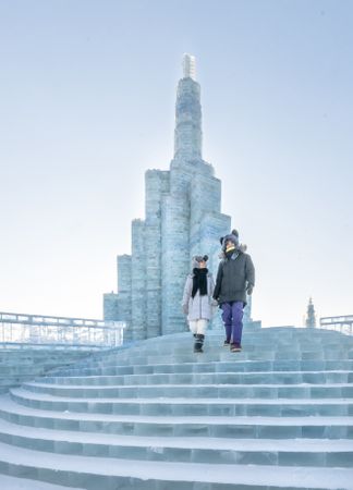 man and woman in warm outwear standing standing on illuminated castle of ice and snow