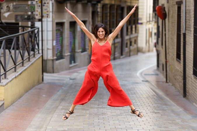 A Joyful Woman Dressed in Red is Energetically Jumping on a Charming City Street