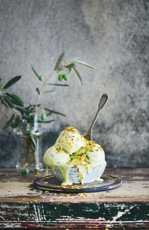 Bowl of melting pistachio ice cream with spoon, and grey background with leaves