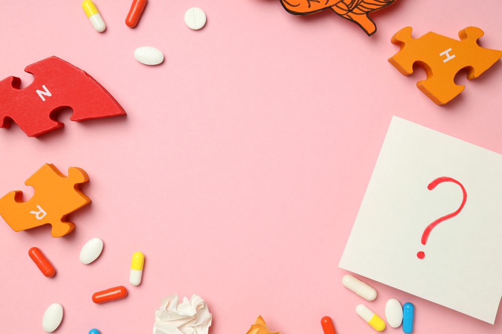Pink paper flat lay with pills, puzzle pieces, brain and question mark with copy space