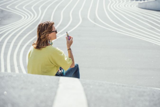 Modern relaxed woman vaping while sitting on marked road