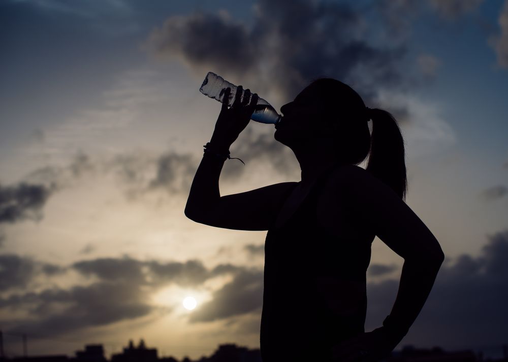 Woman drinking water and sky with clouds at sunset