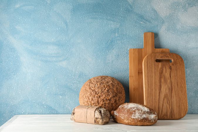 Bakery products and cutting boards on wooden table against light background, space for text