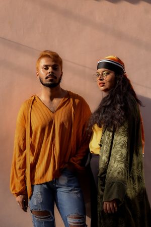 Man and woman wearing casual outfits standing against brown wall