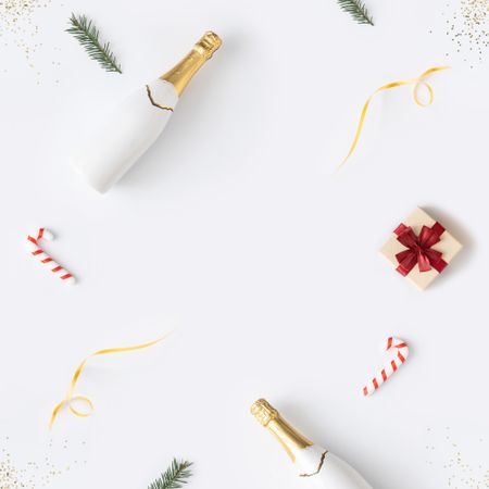 Holiday decorations; Champagne, candy cane and present arranged at top border of light background
