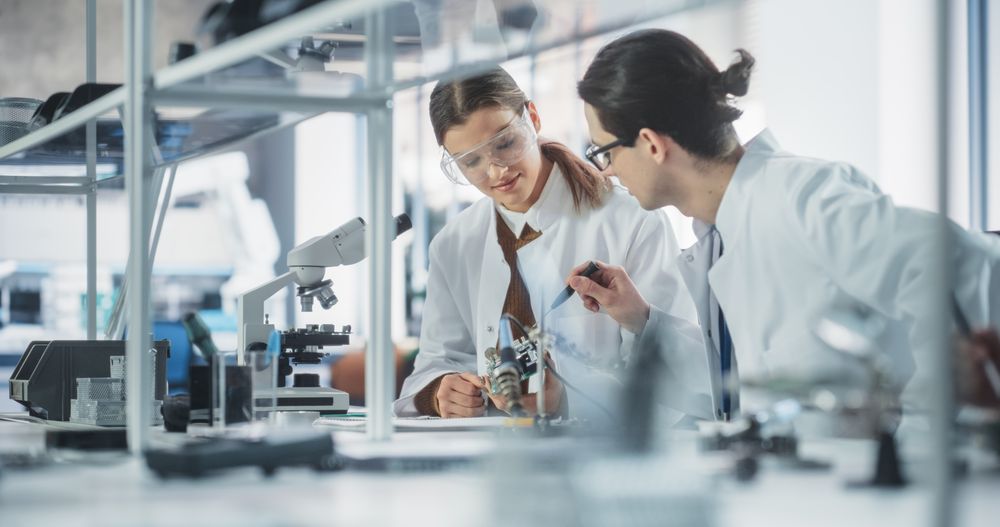 Two Diverse Young Professionals Having a Conversation in a Laboratory, Inspecting a Computer Motherboard with Microchips.