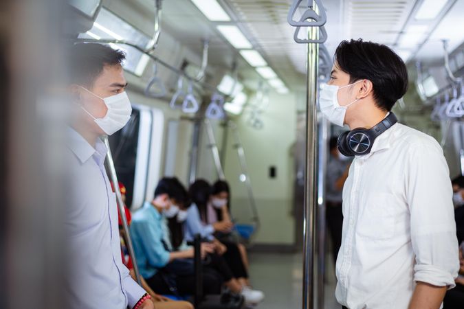 Two men in facemasks chatting in metro car