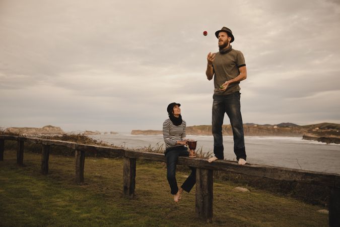 Man juggling balls on bench near woman with drum on shore