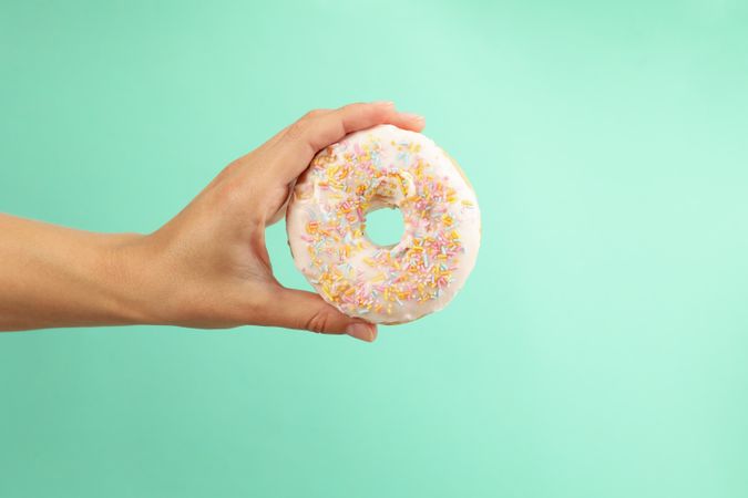 Female hand hold tasty donut on mint background