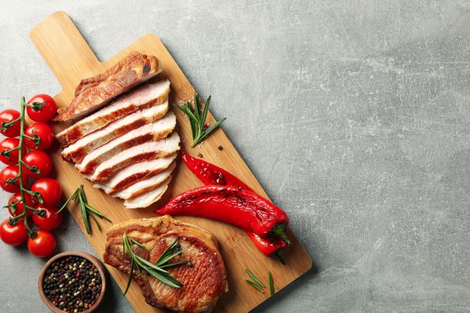 Board with fried steaks on gray background. Grilled food