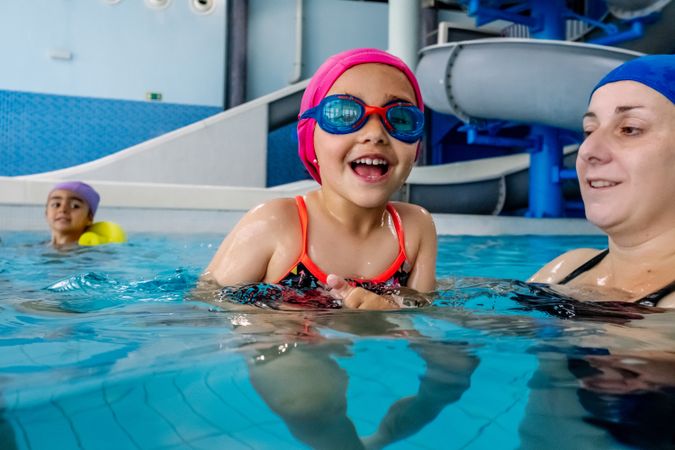 Cheerful girl swimming in pool with mother