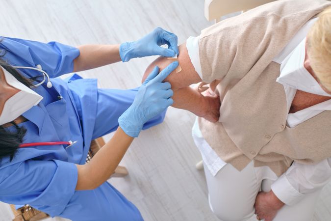 Crop nurse in uniform applying plaster on arm of patient