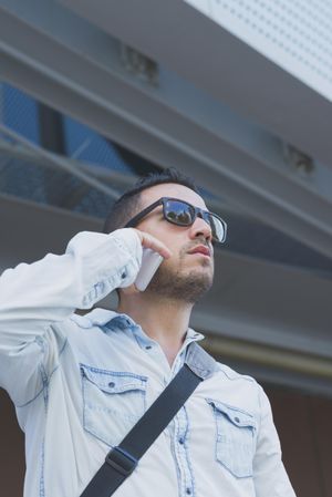 Looking up at male in sunglasses standing with speaking on phone