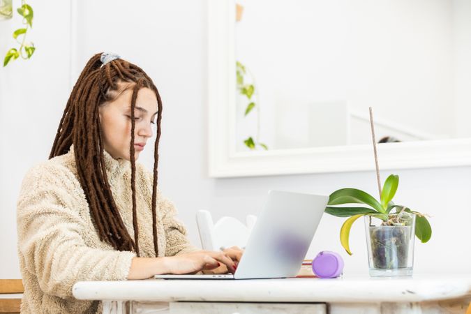 Thoughtful woman with dreadlocks working with a laptop at home