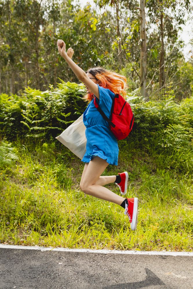 A young person with orange hair jumps happily and contentedly during a walk in a natural rural area