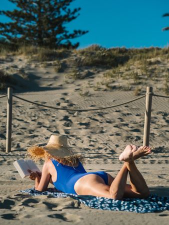 Sandy beach and woman in big hat lying and reading book