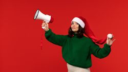 Confident woman in Santa hat raising megaphone with playful look.