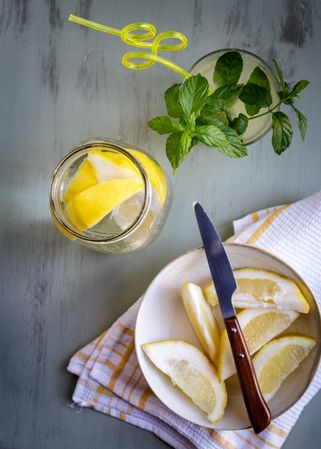 Glass of fresh lemonade next to plate with cut lemons on table