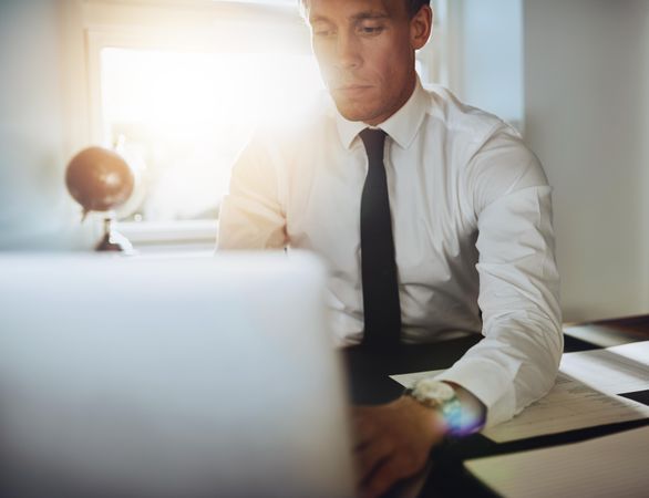 Man in shirt and tie working on laptop in sunny office