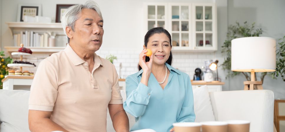 Asian couple playing toss ping pong ball to the cup at home