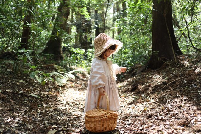 Girl wearing pink dress carrying brown woven basket standing in the woods