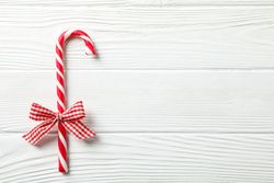 Sweet candy cane with bow on wooden background, space for text