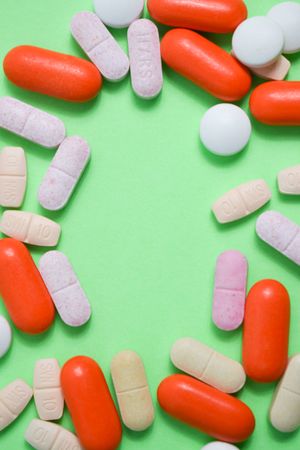 Pills and vitamins surrounding green background with copy space and vertical composition