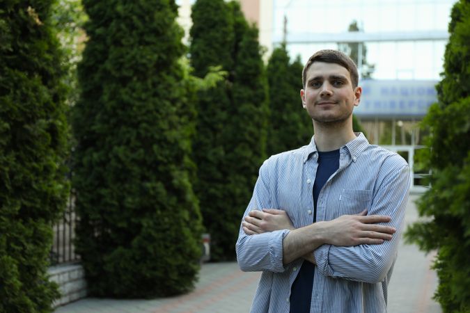 Young man in shirt with folded hands against university. Study