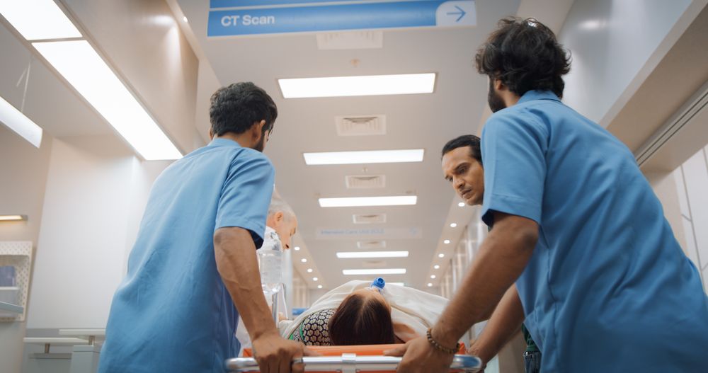 Backview Shot of Group of Medical Specialists Transporting an Older Patient with a Stretcher Through a Hospital Corridor.