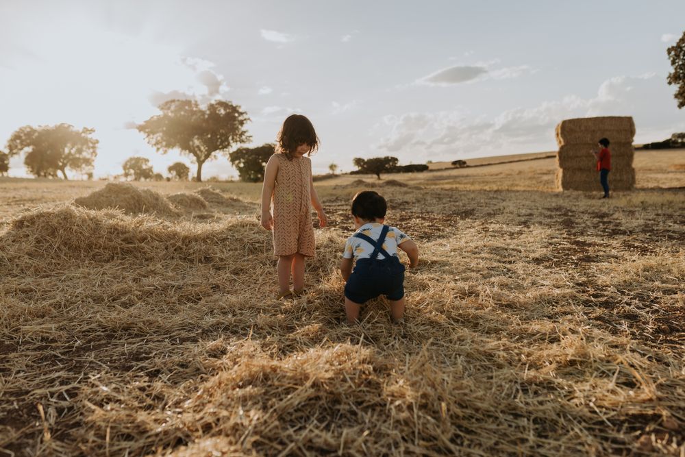 Brother and sister playing in a pile of hay in open field