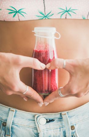 Woman in palm tree crop top holding bottle of small pink smoothie