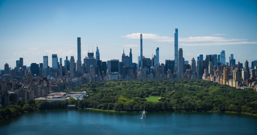 Sunny Weather New York City Aerial Landscape Over Central Park with Midtown Manhattan Skyscrapers. Cinematic Drone View of Urban Skyline with Slightly Cloudy Blue Sky