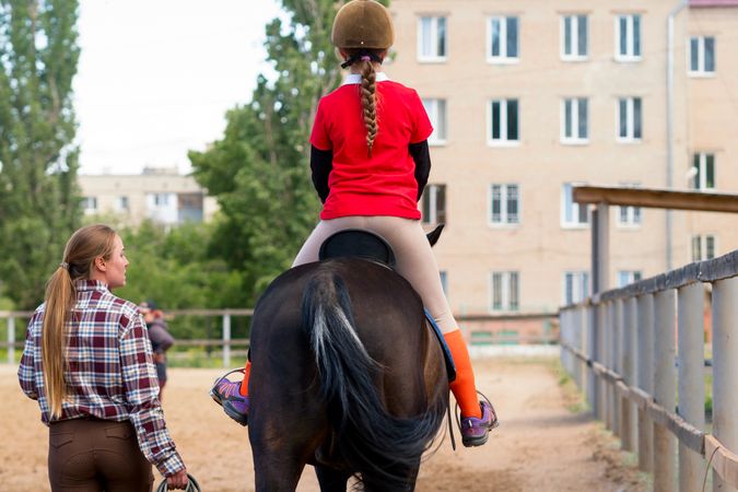 Instructor leads young rider on horse during outdoor training.