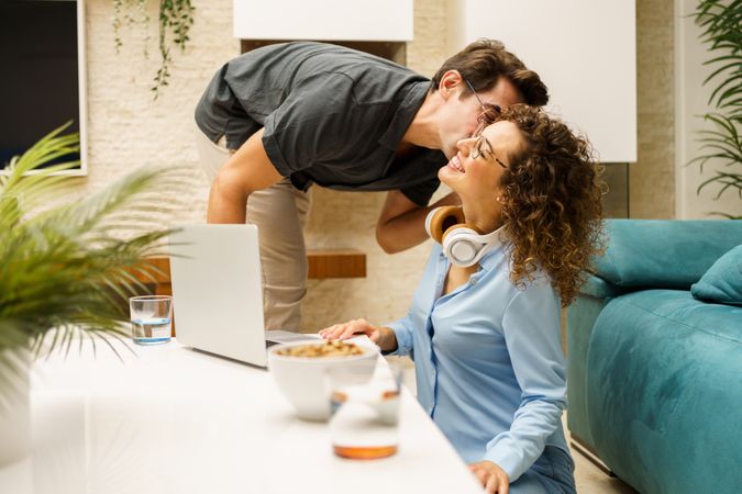 Happy couple with laptop having fun while working remotely in living room