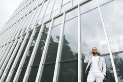 Elegant Black man talking smartphone leaning building
