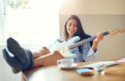 Woman having fun and smiling while playing guitar at her desk