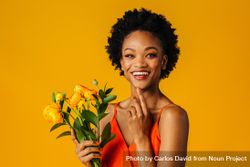 Happy Black woman holding a ranunculus bouquet with a finger to her chin 5okwk5