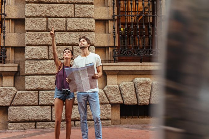 Tourist couple using a map to find their destination while pointing up